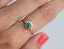 Emerald and diamond ring on finger, showcasing 0.4ct Emerald with diamond halo.