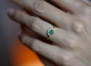 Emerald and diamond ring on hand, showcasing green gemstone and halo design.